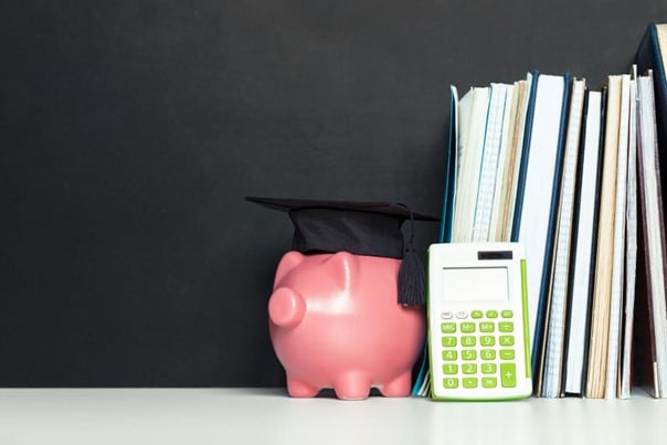 Imagem de cofrinho em formato de porco com chapéu de formatura, com livros e calculadora ao lado